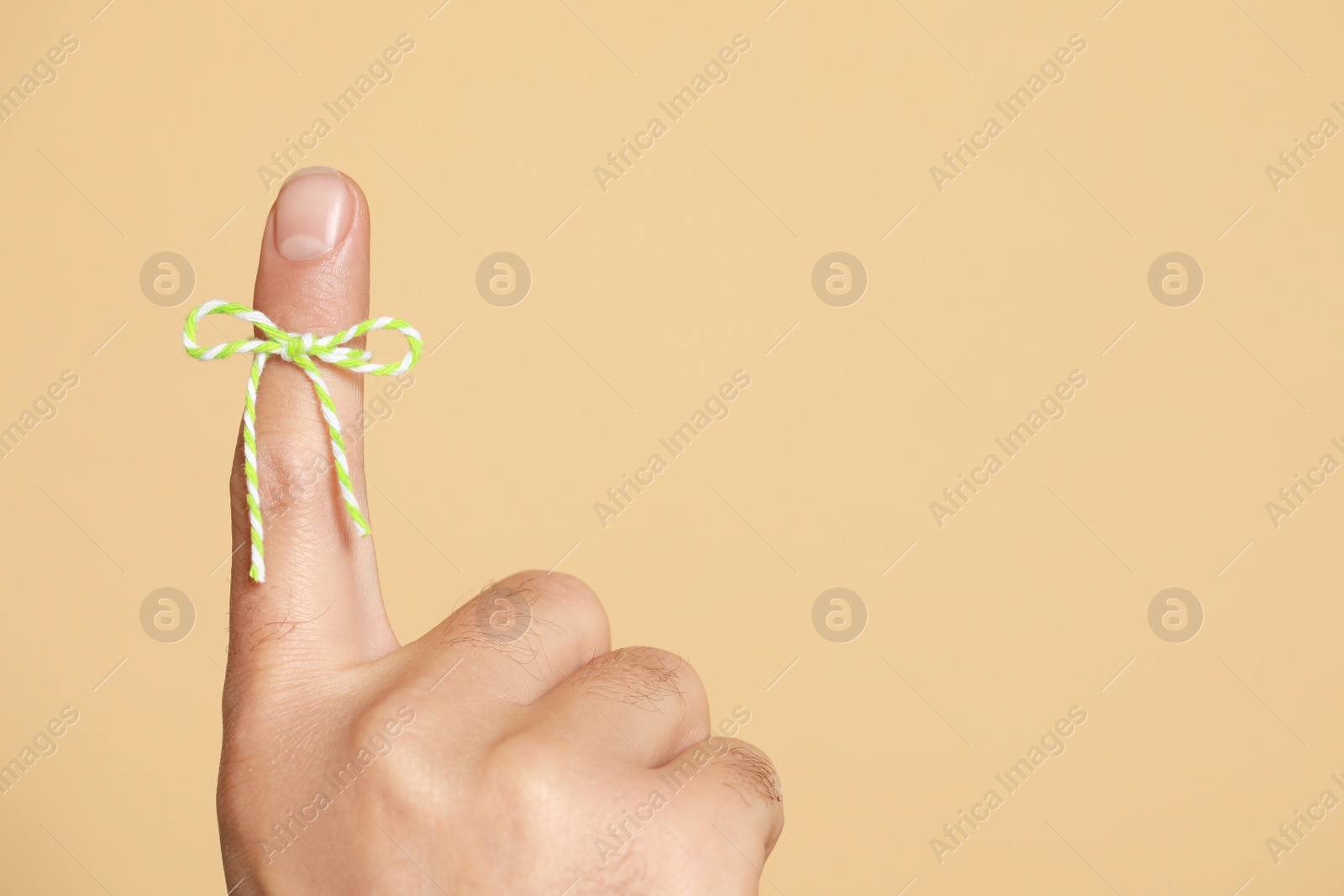 Photo of Man showing index finger with tied bow as reminder on beige background, closeup. Space for text