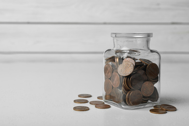 Glass jar with coins on white table, space for text