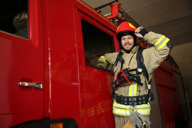 Portrait of firefighter in uniform near red fire truck at station