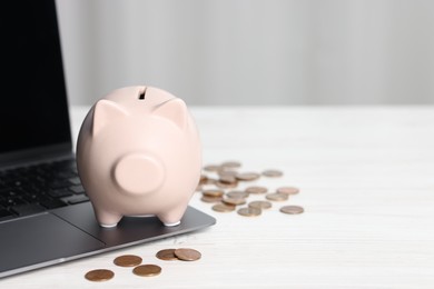 Photo of Piggy bank, coins and laptop on white table indoors. Space for text