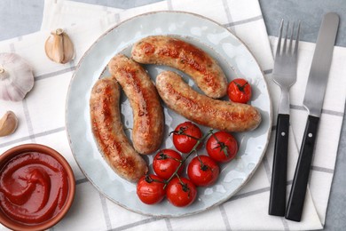 Photo of Tasty homemade sausages, tomatoes, garlic and ketchup on grey textured table, flat lay