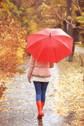 Woman with umbrella taking walk in autumn park on rainy day