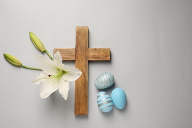 Wooden cross, painted Easter eggs and lily flowers on grey background, flat lay. Space for text