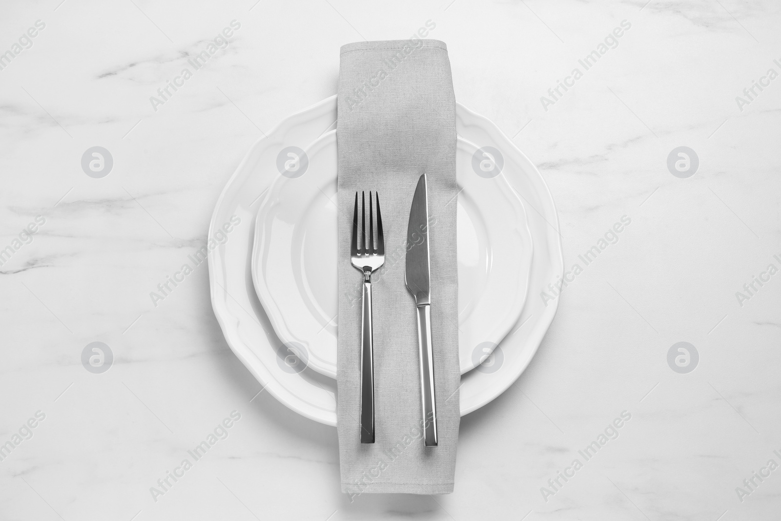 Photo of Clean plates with shiny silver cutlery on white marble table, flat lay