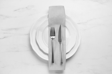 Photo of Clean plates with shiny silver cutlery on white marble table, flat lay