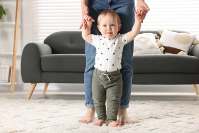 Photo of Mother supporting her baby son while he learning to walk on carpet at home