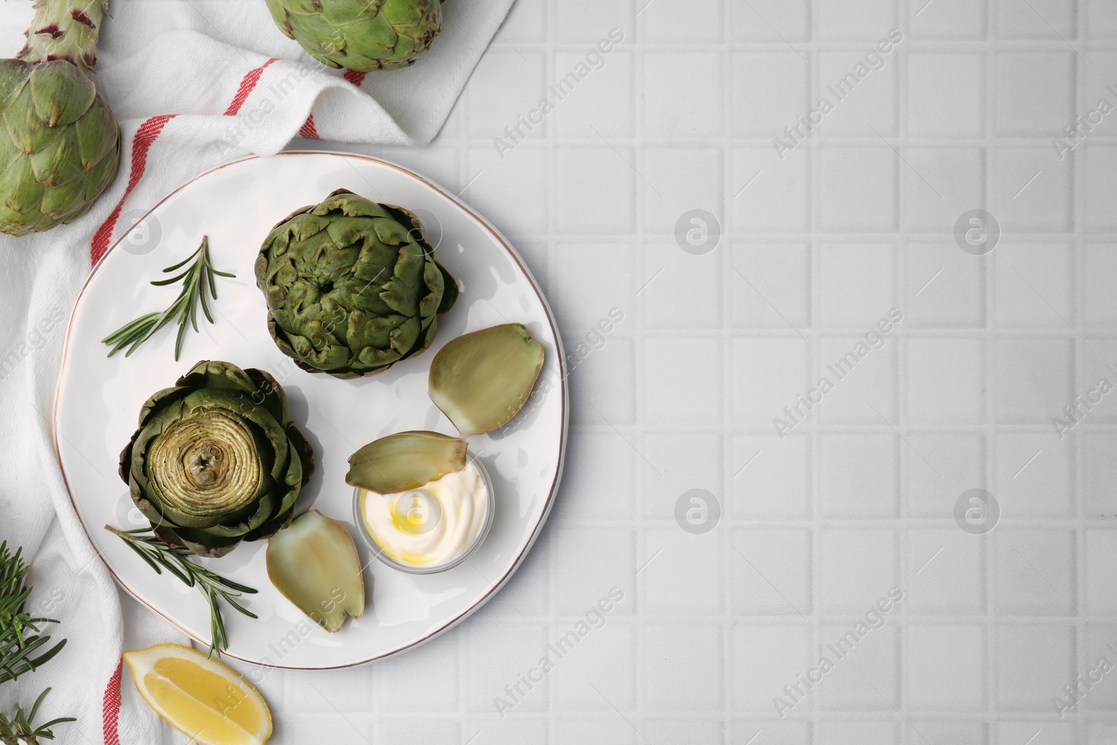 Photo of Delicious cooked artichokes with tasty sauce served on white tiled table, flat lay. Space for text