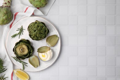Delicious cooked artichokes with tasty sauce served on white tiled table, flat lay. Space for text