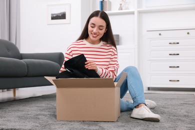 Happy young woman taking black jeans out of box at home. Online shopping