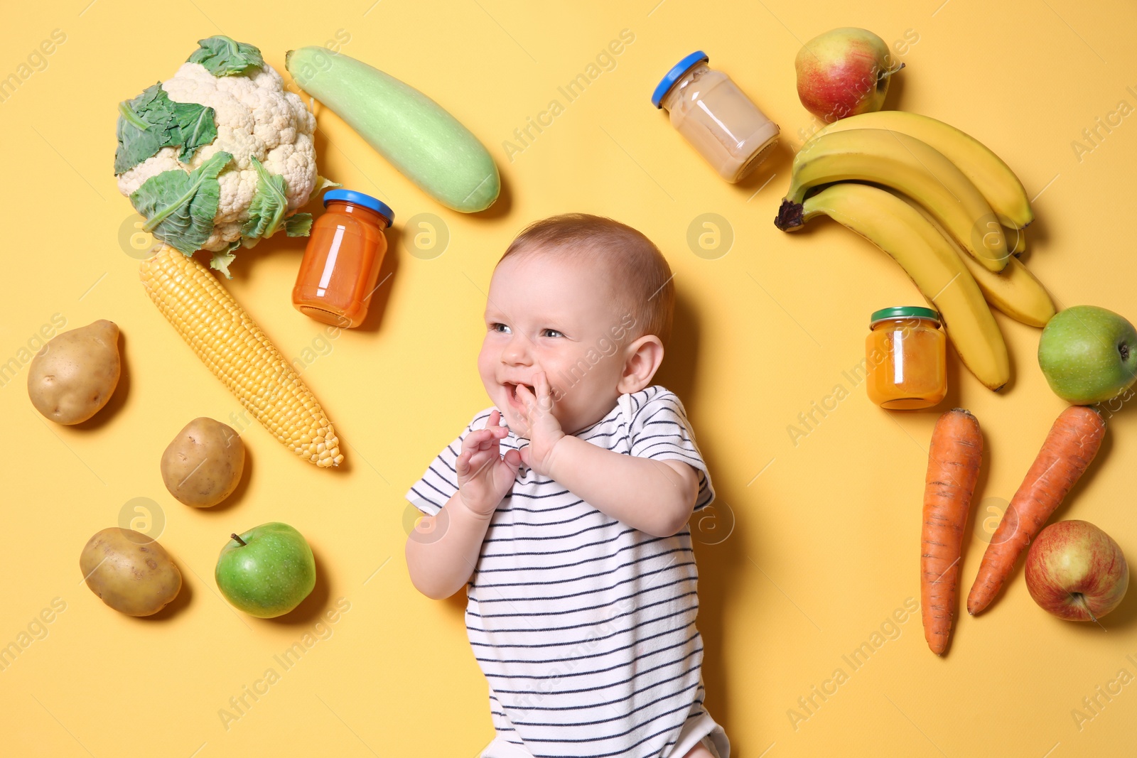 Photo of Cute little child with ingredients and purees in jars on color background, top view. Baby food