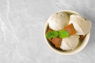 Bowl of delicious ice cream with caramel candies and mint on light grey marble table, top view. Space for text