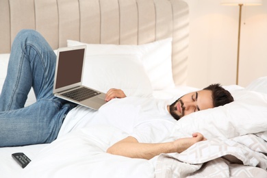 Lazy young man with laptop sleeping on bed at home