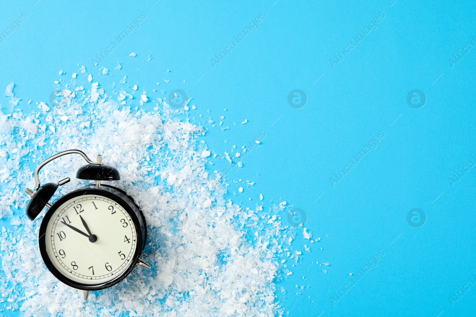 Photo of Alarm clock and snow on light blue background, flat lay with space for text. New Year countdown