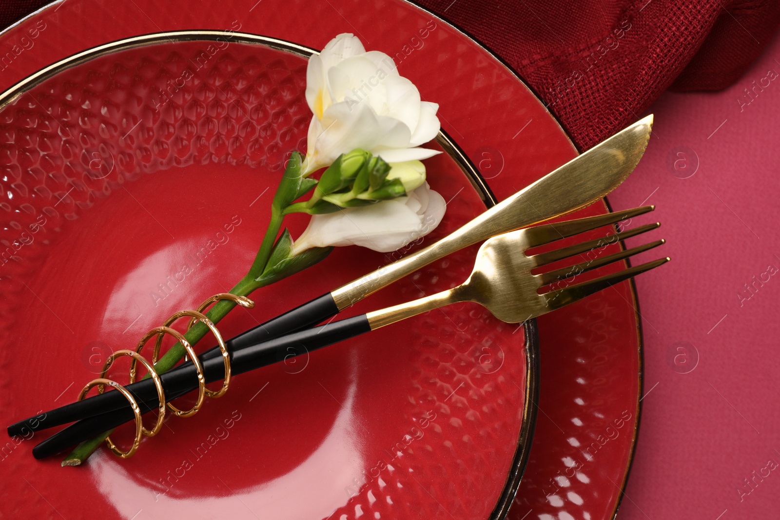 Photo of Stylish table setting with cutlery and floral decor on pink background, top view