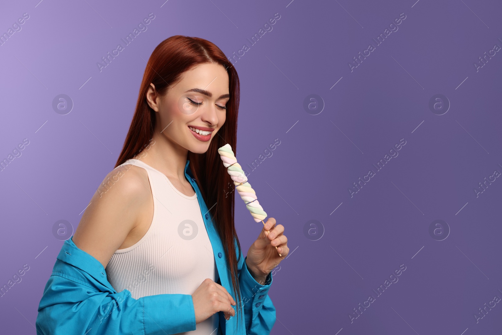 Photo of Happy woman with red dyed hair and marshmallows on purple background, space for text