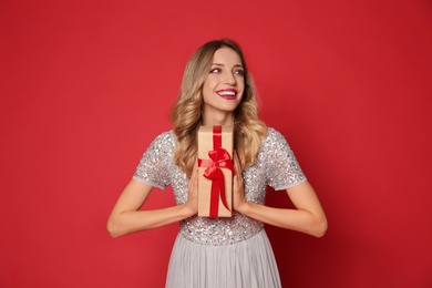 Happy woman with gift box on red background. Christmas party
