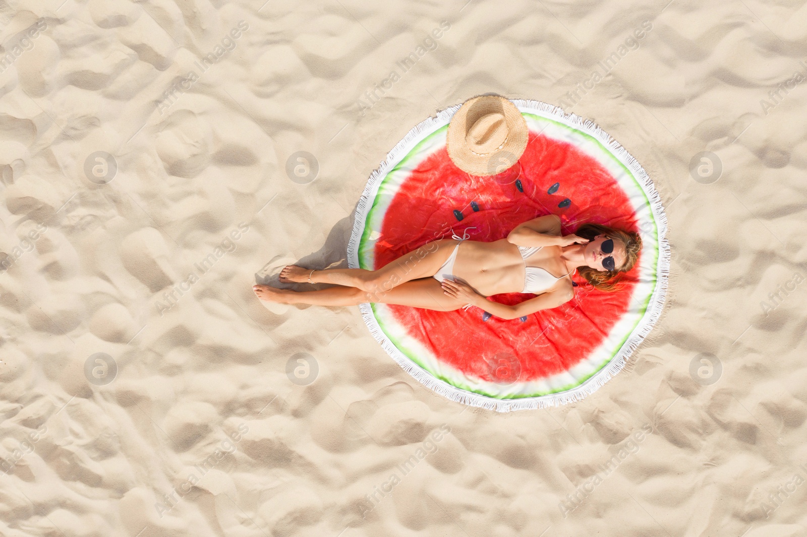 Image of Woman sunbathing on round beach towel at sandy coast, aerial view