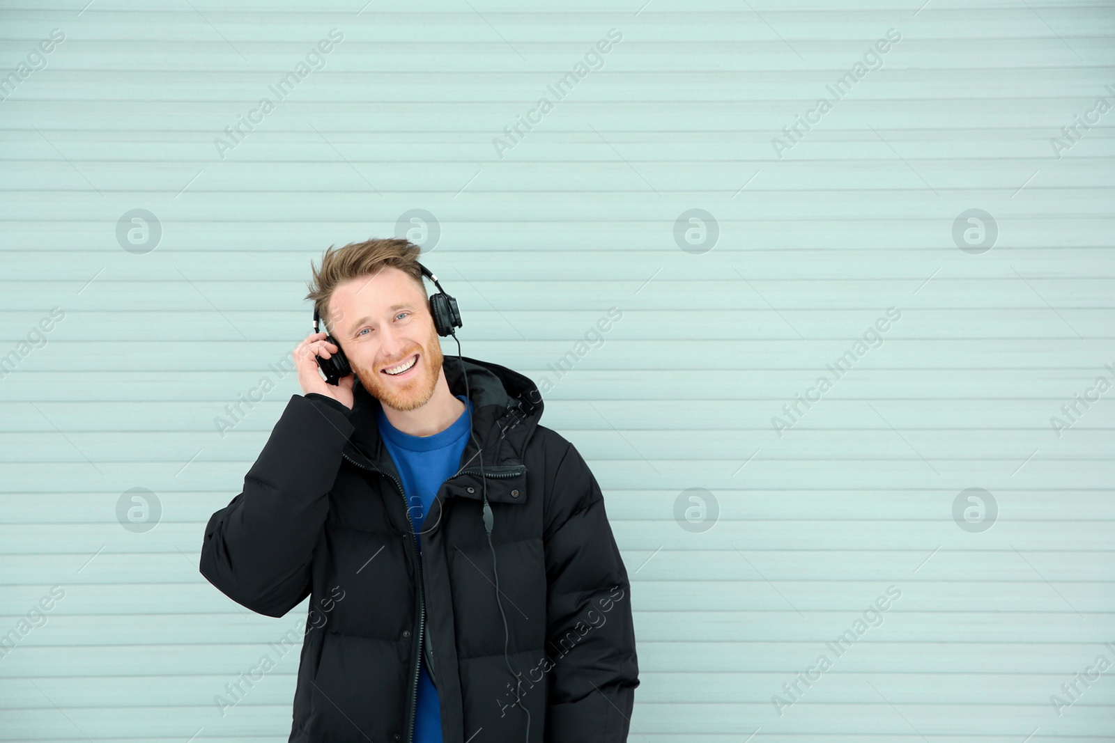 Photo of Young man listening to music with headphones against light wall. Space for text