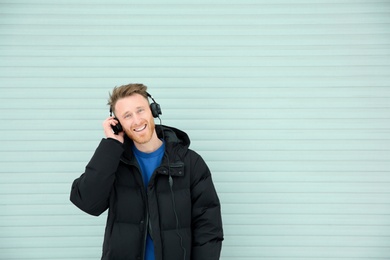 Photo of Young man listening to music with headphones against light wall. Space for text