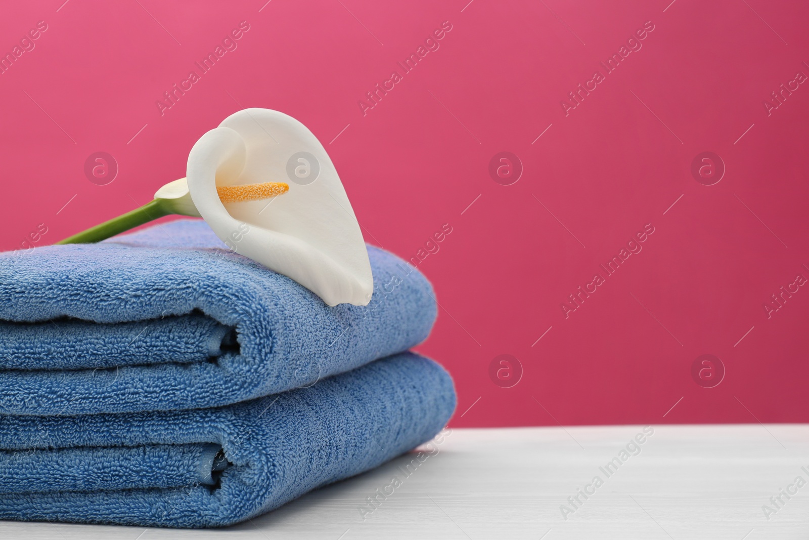 Photo of Soft clean towels with beautiful flower on table against color background. Space for text