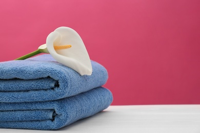 Photo of Soft clean towels with beautiful flower on table against color background. Space for text