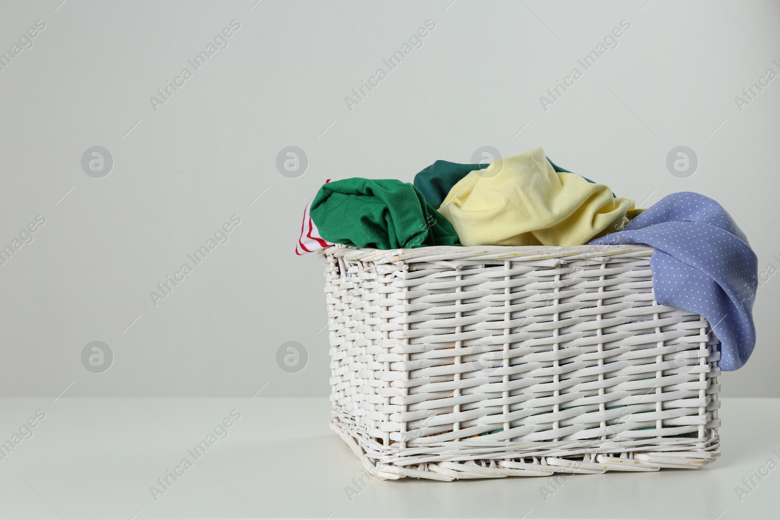 Photo of Wicker laundry basket with different clothes on light background. Space for text