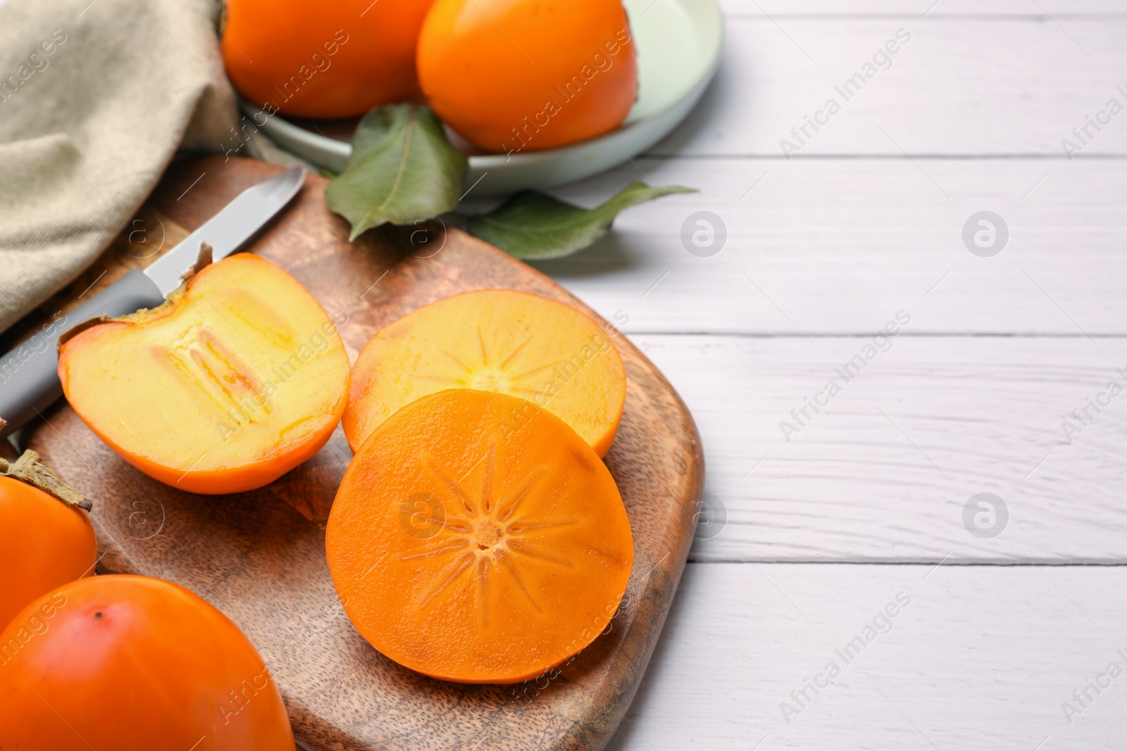 Photo of Delicious ripe juicy persimmons and knife on white wooden table, space for text