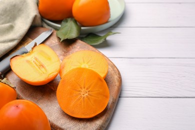 Photo of Delicious ripe juicy persimmons and knife on white wooden table, space for text