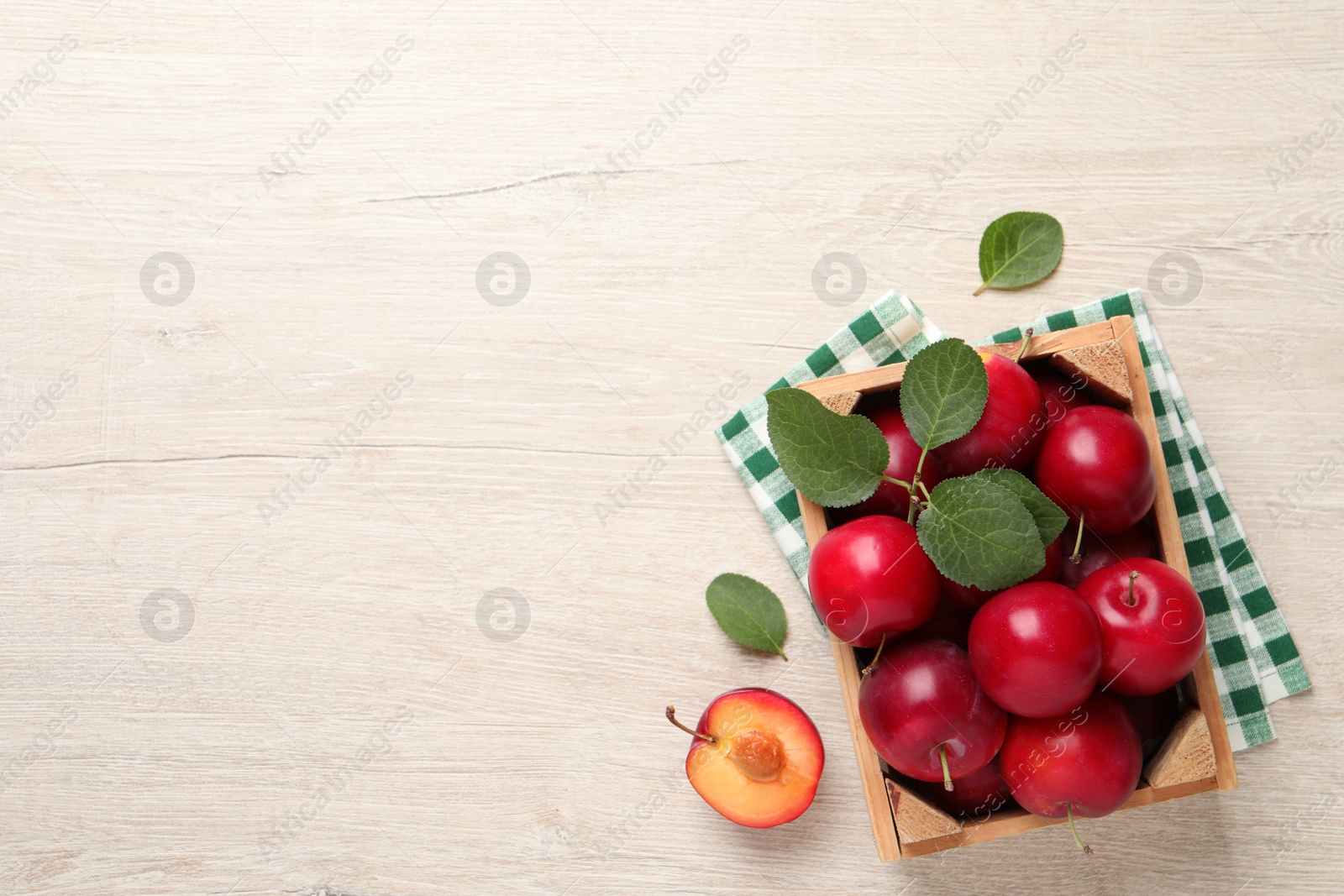 Photo of Delicious ripe cherry plums with leaves on white wooden table, flat lay. Space for text