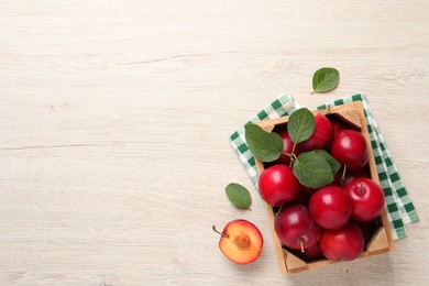 Photo of Delicious ripe cherry plums with leaves on white wooden table, flat lay. Space for text