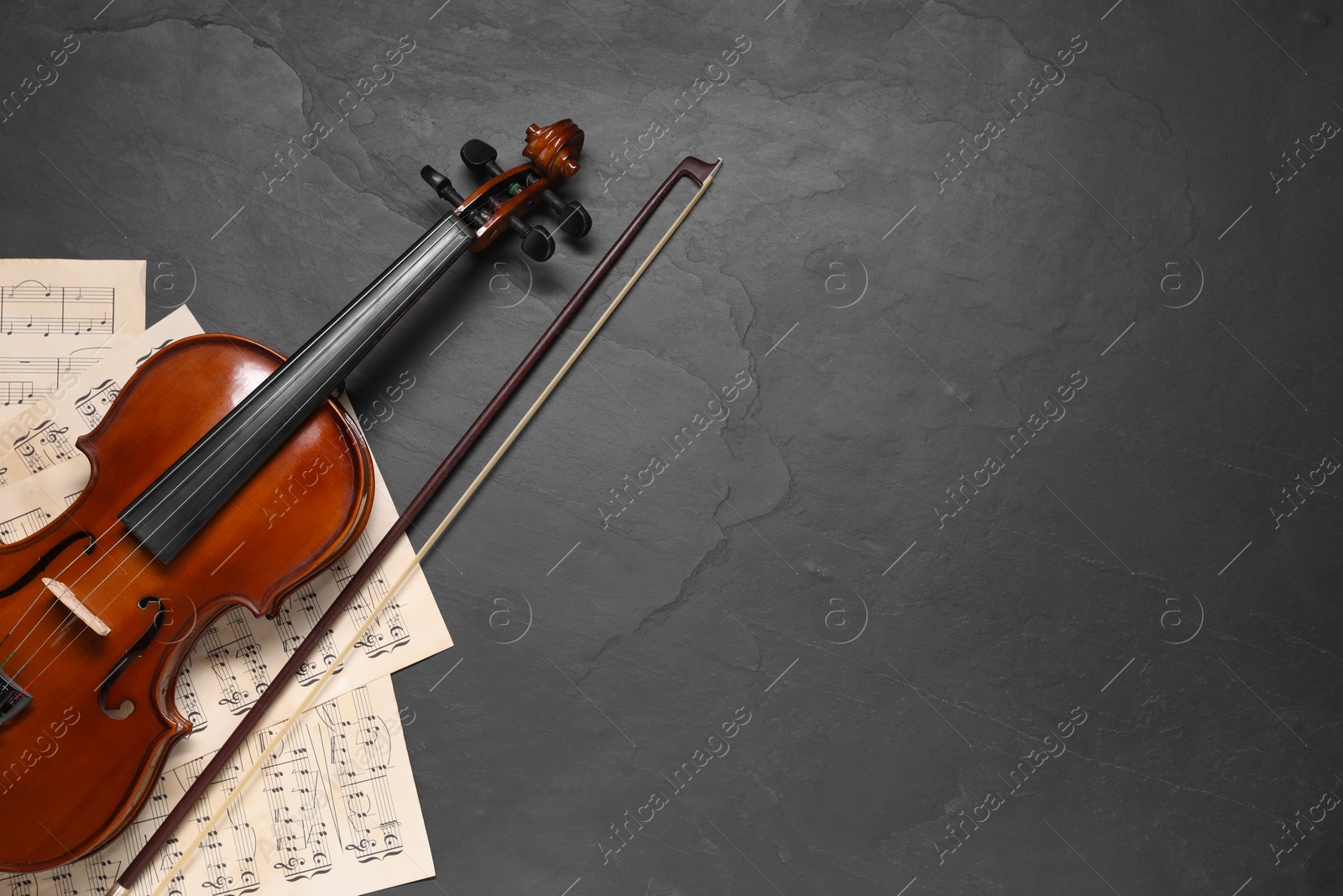 Photo of Violin, bow and music sheets on black table, top view. Space for text