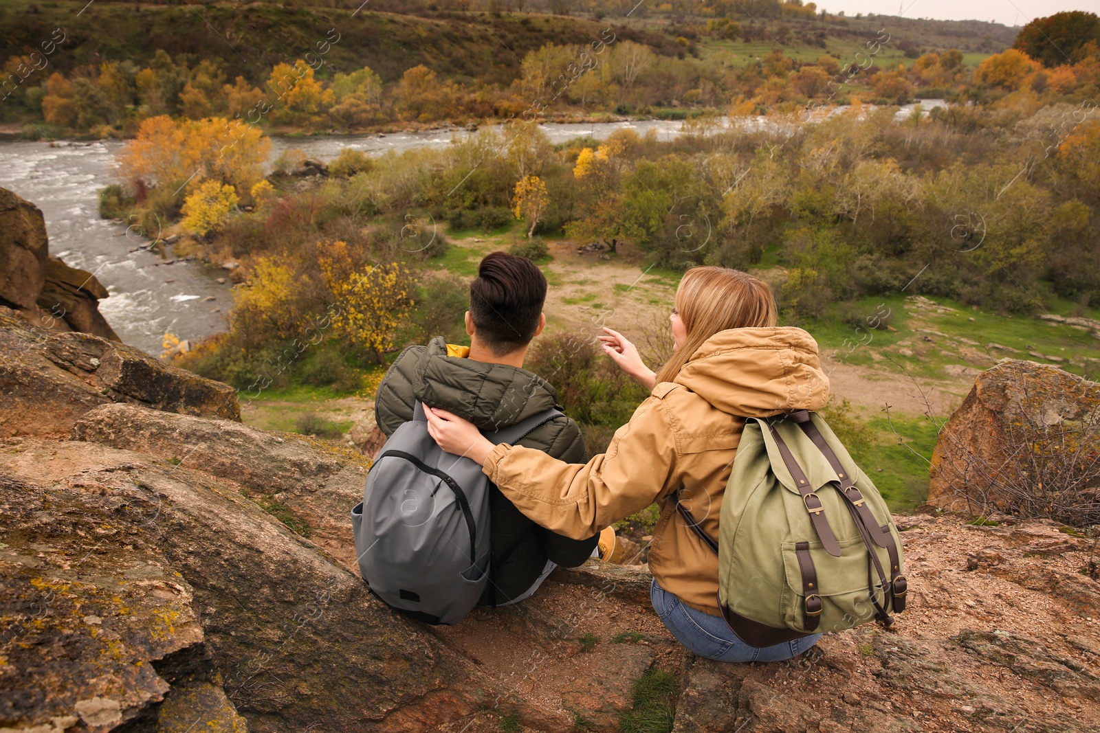 Photo of Couple of hikers with travel backpacks enjoying beautiful view near mountain river