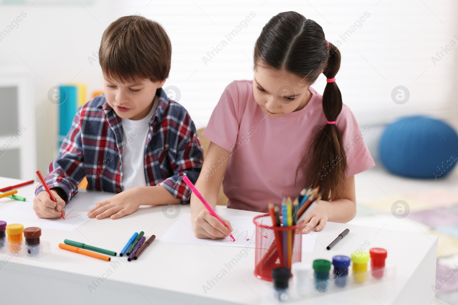 Photo of Happy brother and sister drawing at white table in room