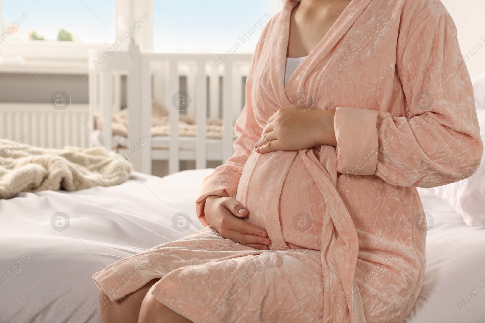 Photo of Pregnant woman in bathrobe on bed at home, closeup