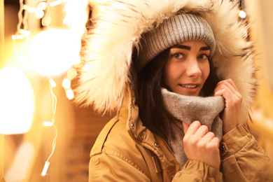 Photo of Beautiful young woman near festive lights outdoors. Winter vacation