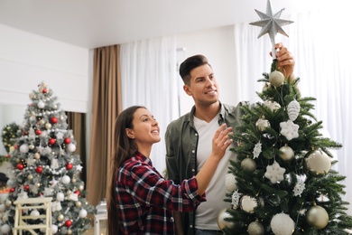 Couple decorating Christmas tree with star topper in room