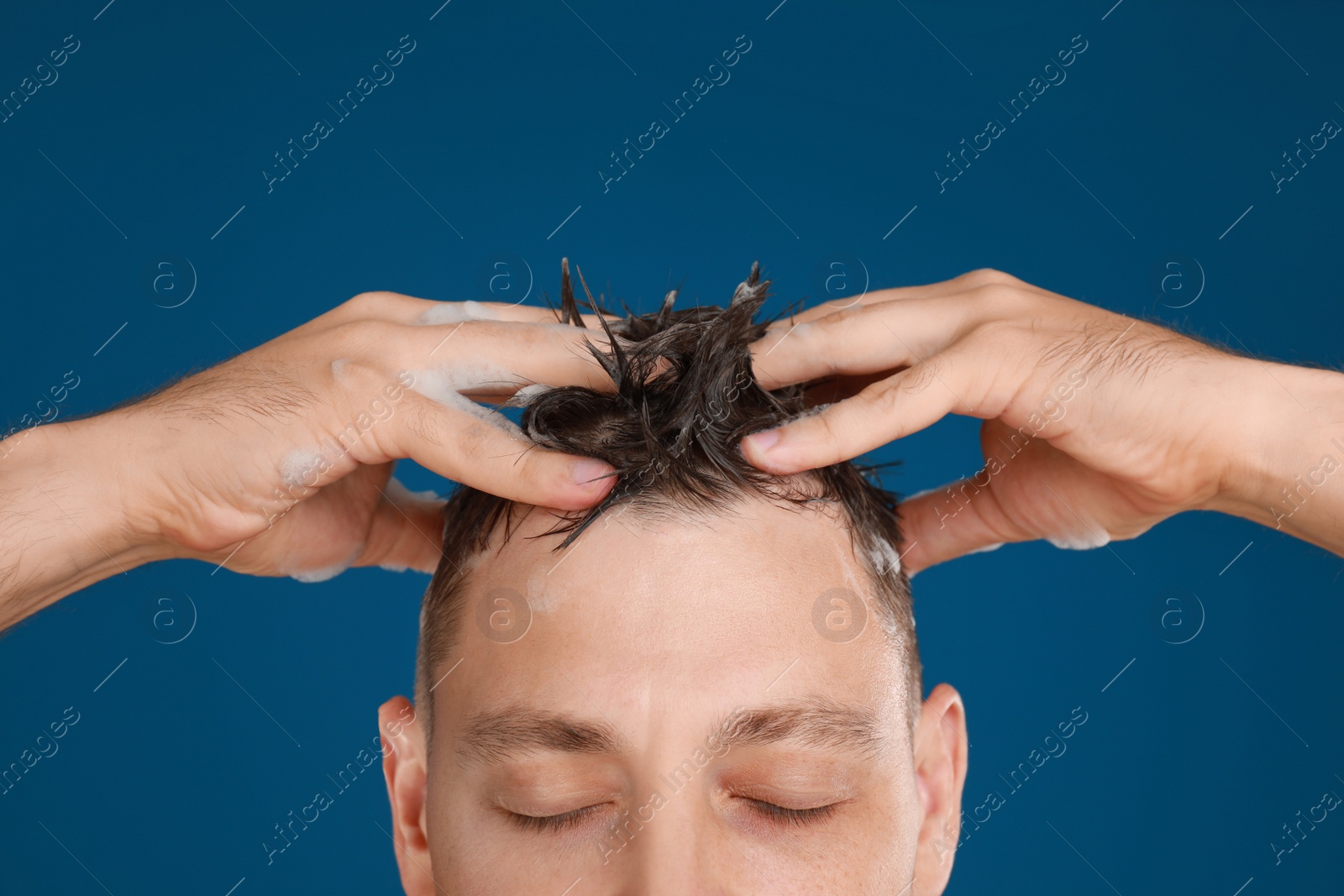 Photo of Man washing hair on blue background, closeup