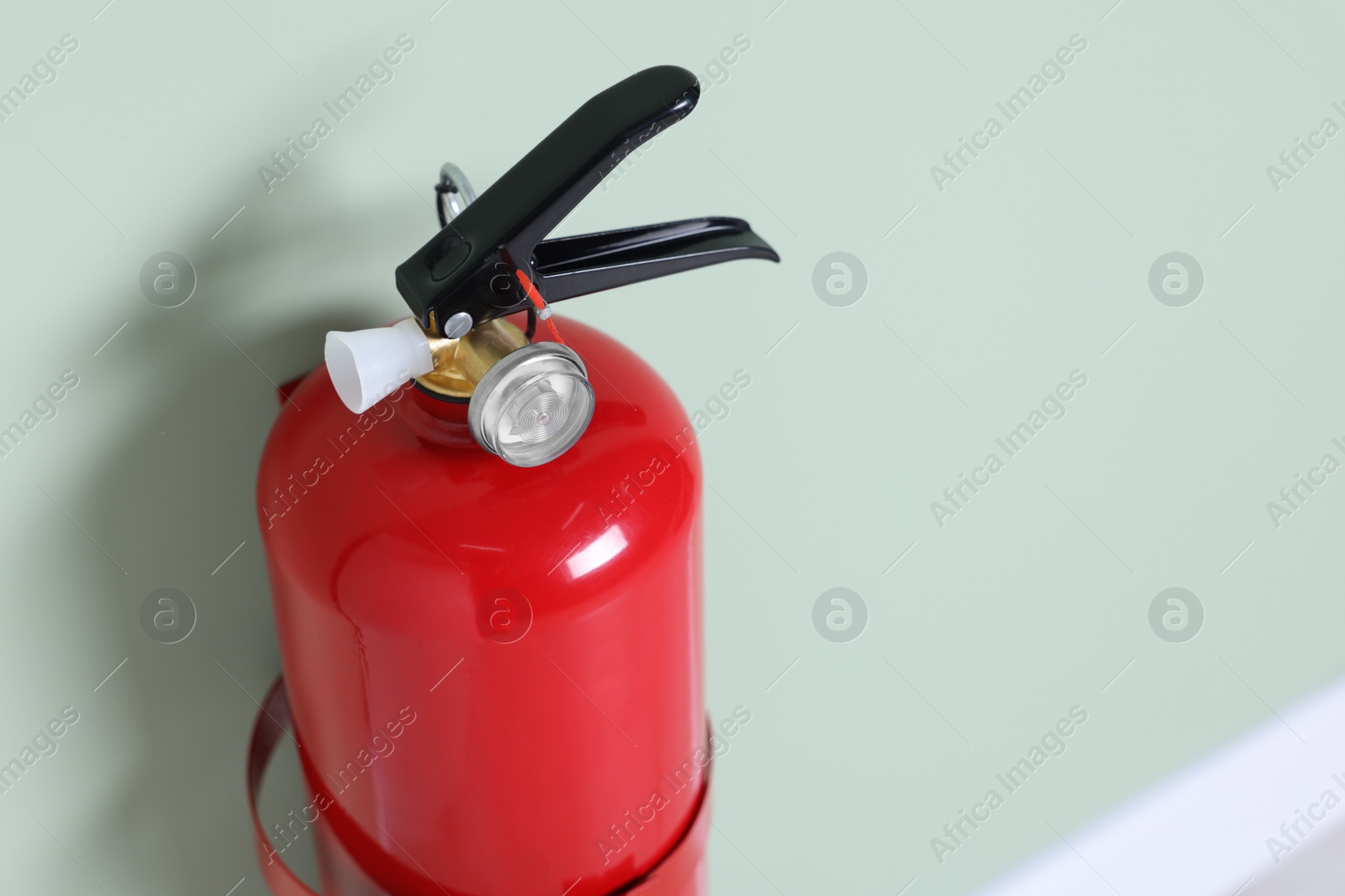 Photo of Red fire extinguisher on light green wall, closeup. Space for text
