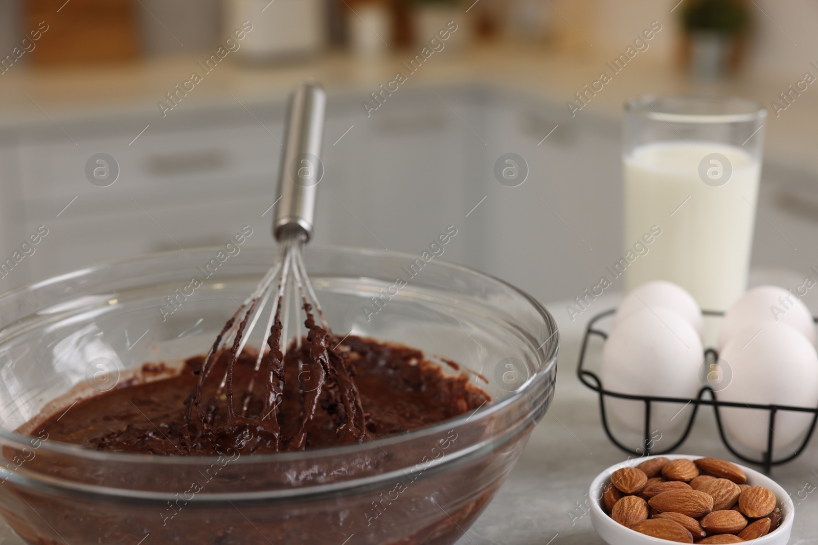 Photo of Metal whisk, chocolate cream in bowl and different products on gray table indoors, closeup