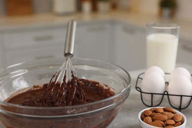 Photo of Metal whisk, chocolate cream in bowl and different products on gray table indoors, closeup