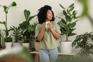 Relaxing atmosphere. Happy woman with cup of hot drink near beautiful houseplants in room