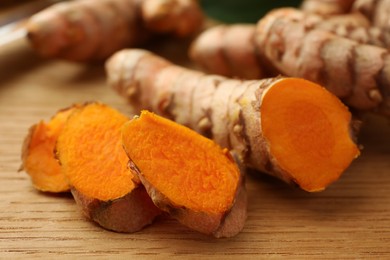 Photo of Cut turmeric roots on wooden table, closeup