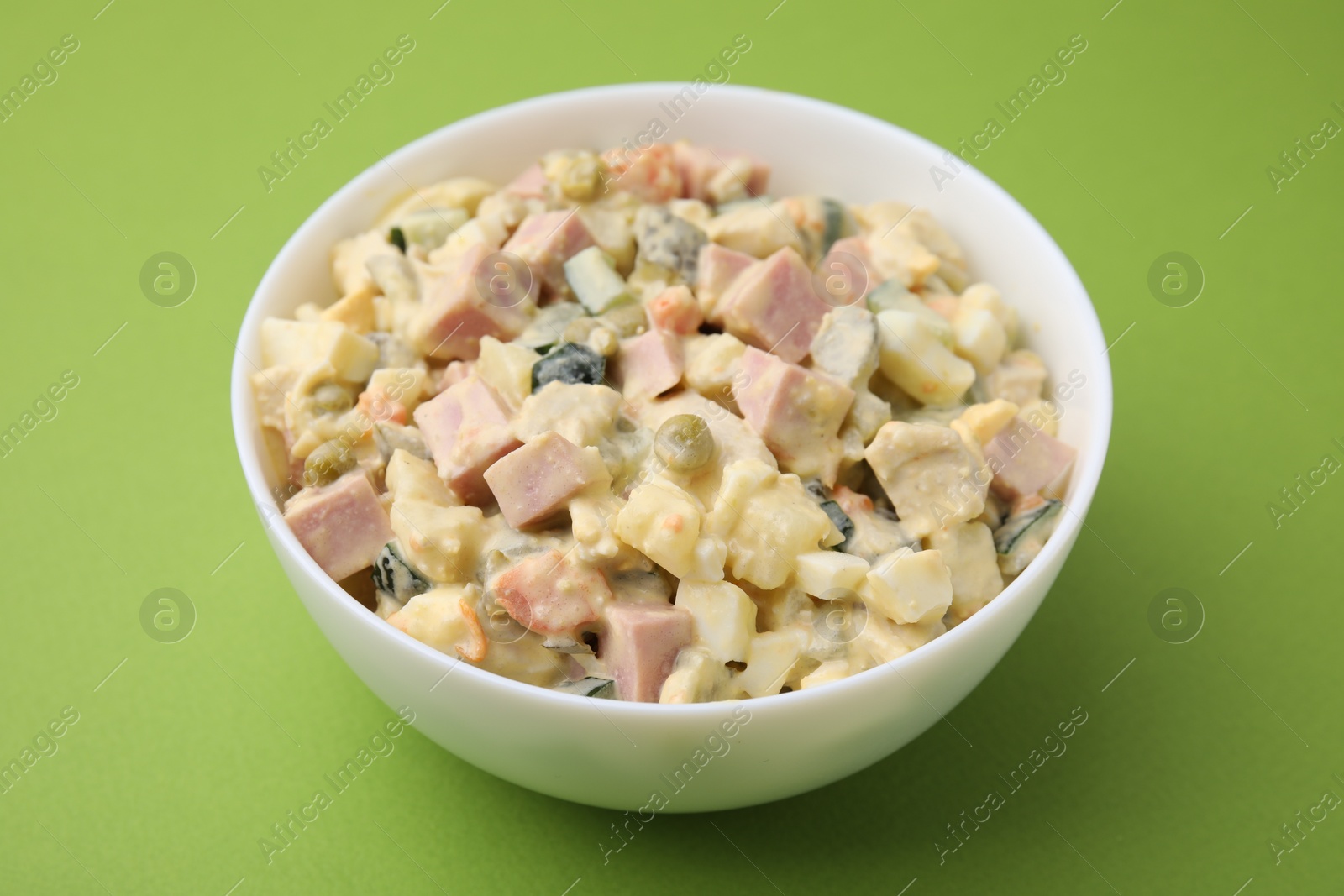 Photo of Tasty Olivier salad with boiled sausage in bowl on green table