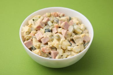 Tasty Olivier salad with boiled sausage in bowl on green table