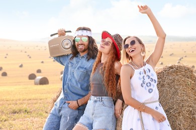 Photo of Happy hippie friends with radio receiver near hay bale in field