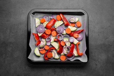 Photo of Baking pan with parchment paper and raw vegetables on dark grey table, top view