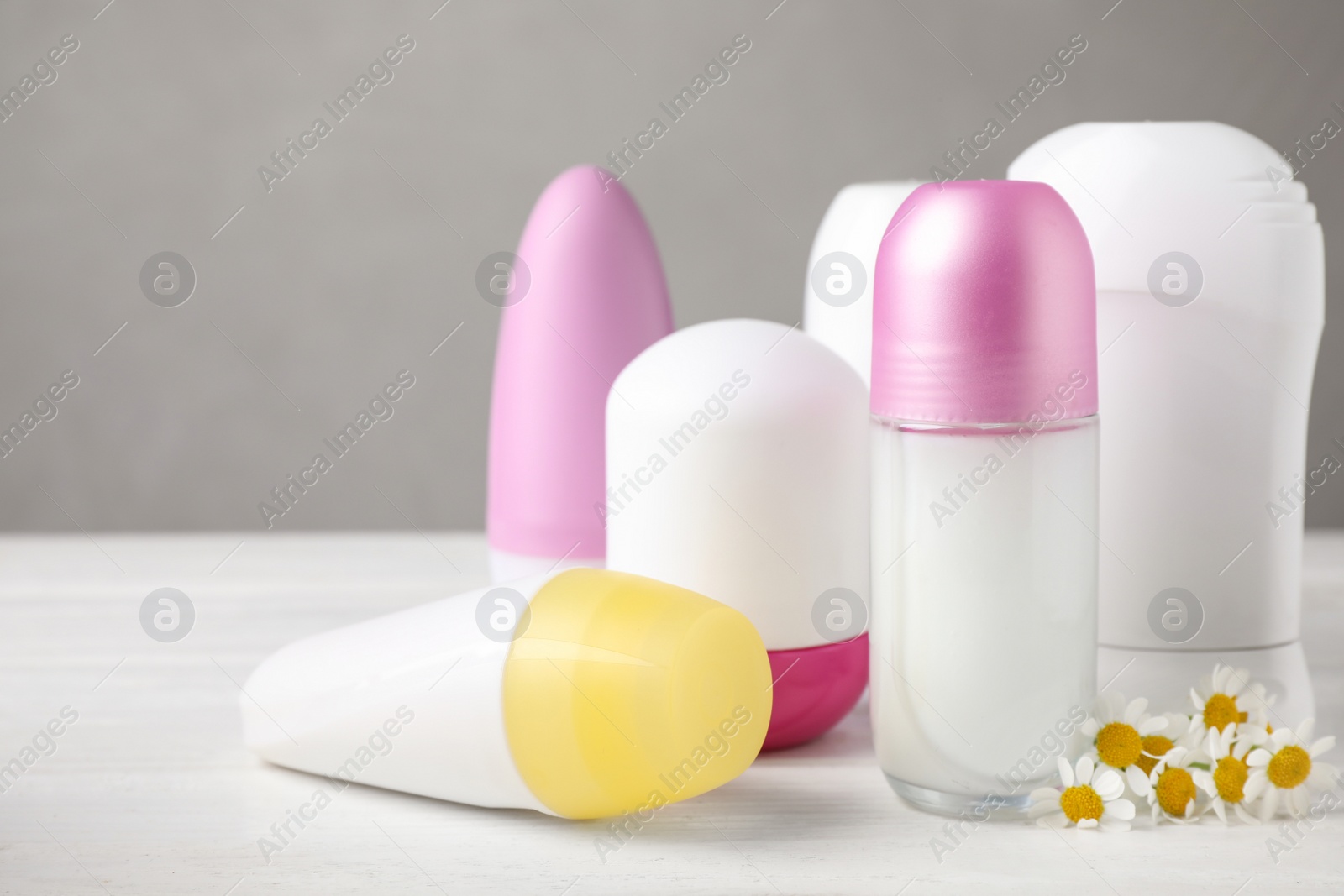 Photo of Natural female roll-on deodorants and chamomile flowers on white table