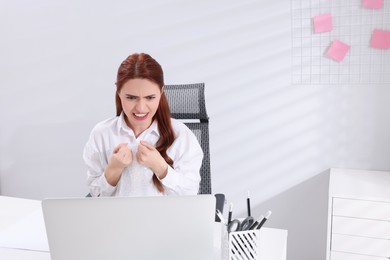 Photo of Angry woman popping bubble wrap at desk in office, space for text. Stress relief