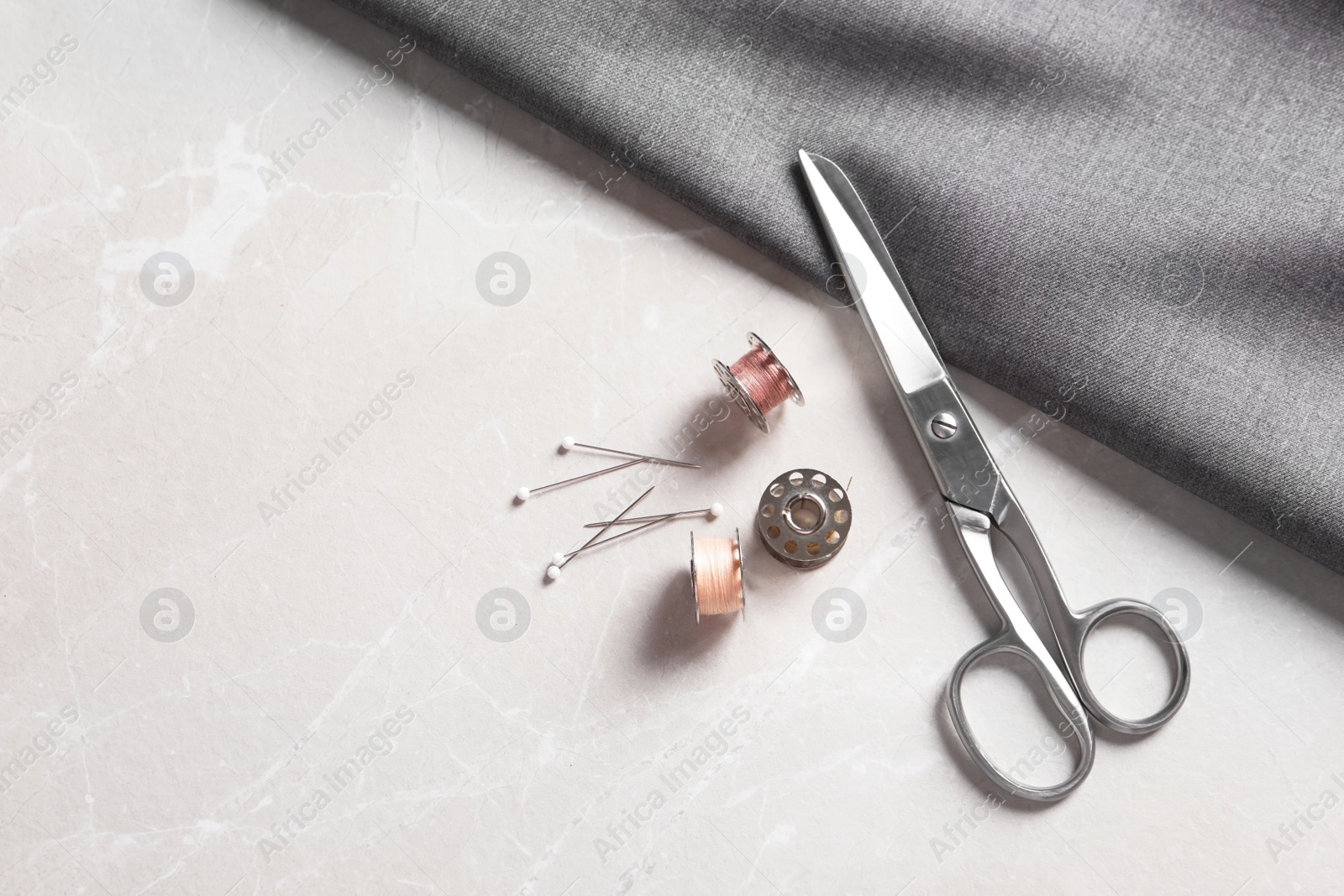 Photo of Bobbins with threads, fabric and scissors on table, top view. Tailoring accessories