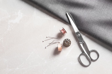 Photo of Bobbins with threads, fabric and scissors on table, top view. Tailoring accessories